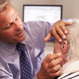 Doctor Fitting Senior Female Patient With Hearing Aid