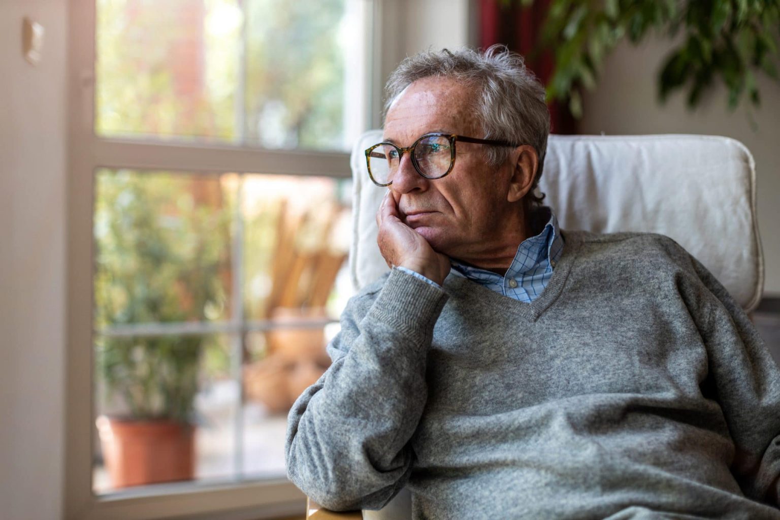 Older man looking outside the window of his home.