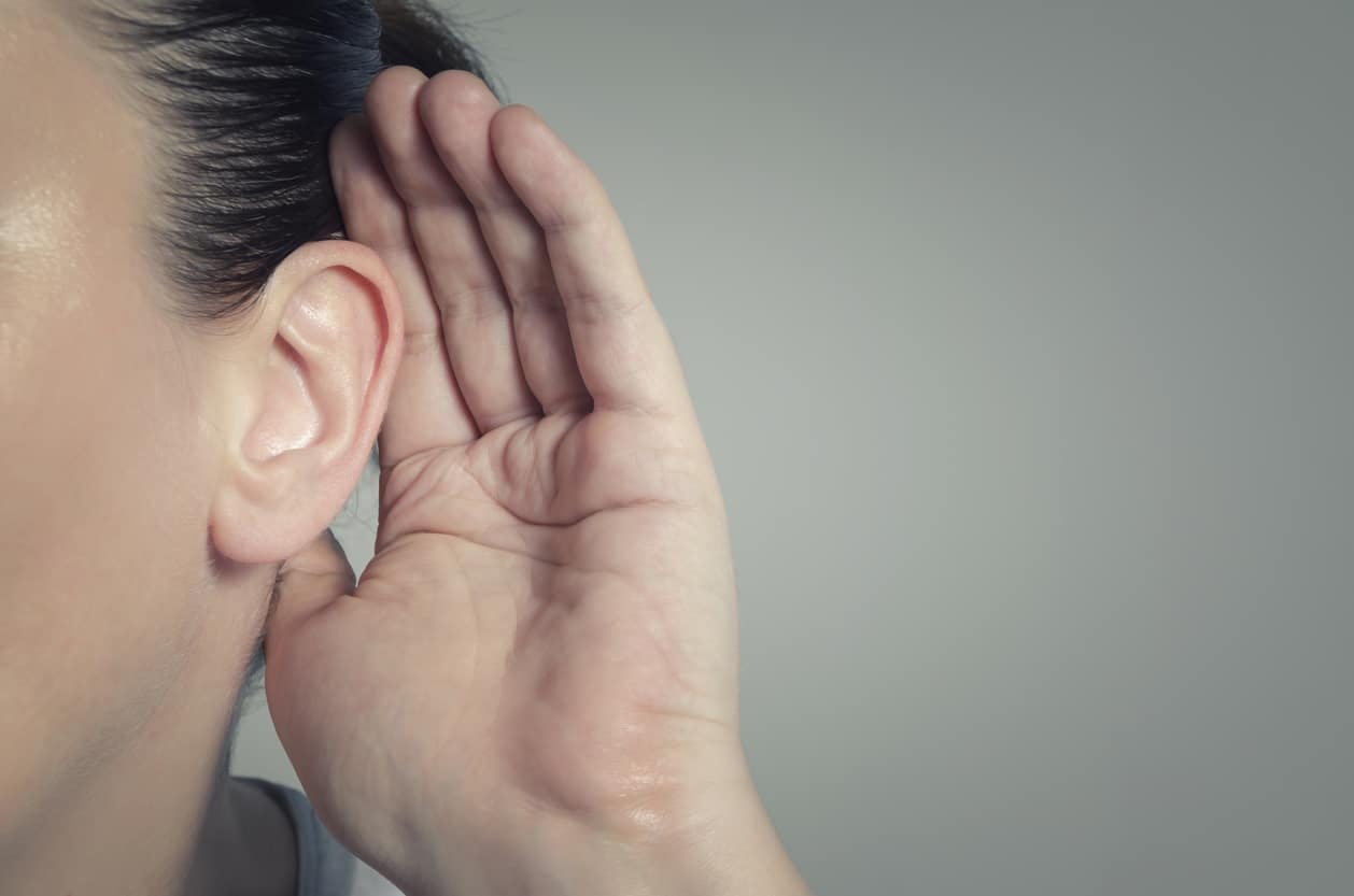 Woman cupping her ear with hear hand to try and hear better.