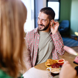 Smiling man wearing hearing aids while sitting at the kitchen table and talking with his family
